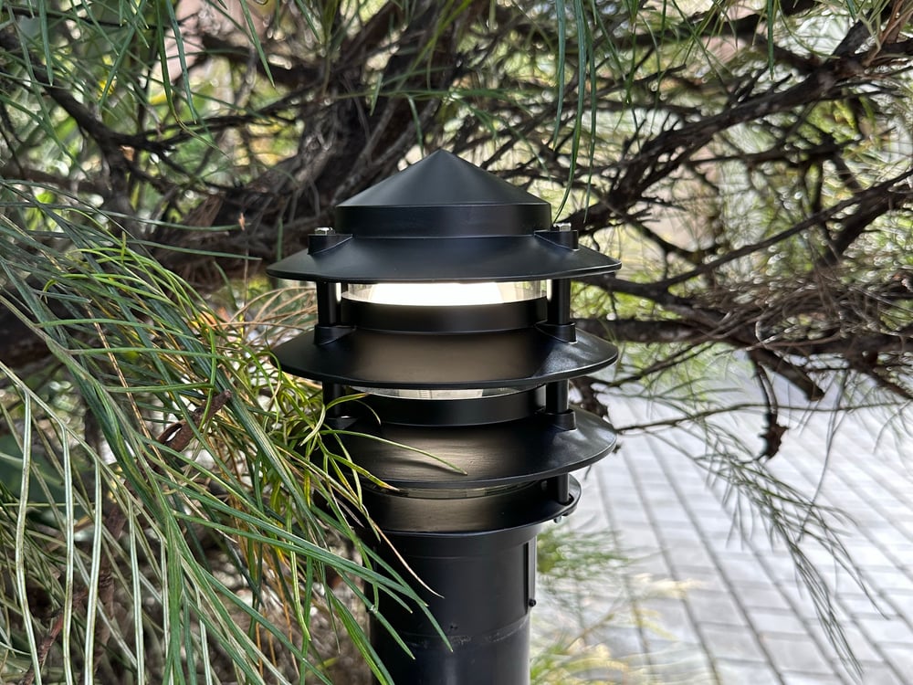 Illuminated black outdoor garden bollard light along a paved pathway